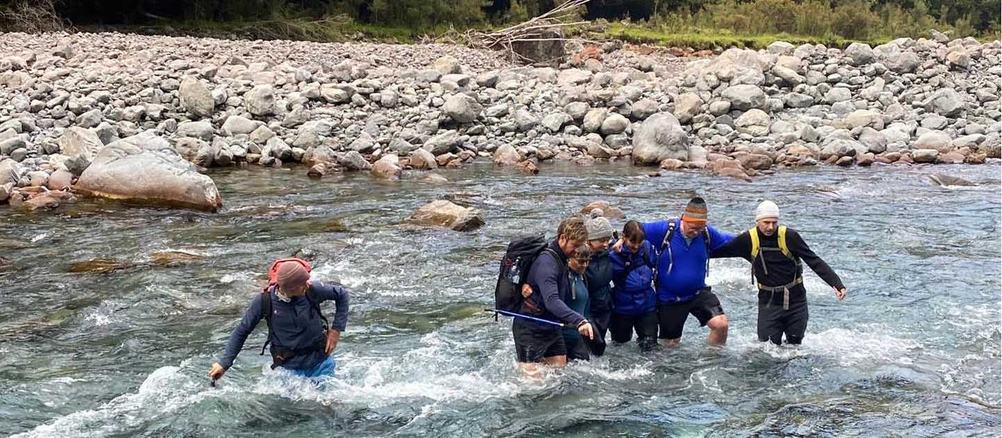 Linking arms, crossing the Deception River over Goat Pass. | Adventure South NZ